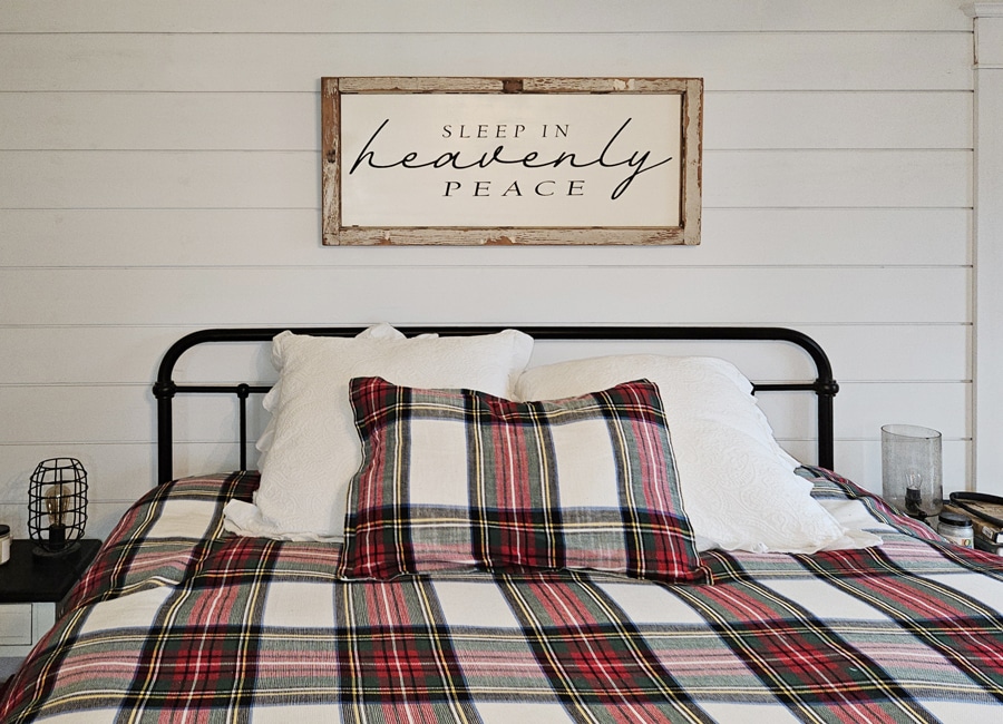 Bed with plaid sheets against a shiplap wall with sleep in heavenly peace sign above