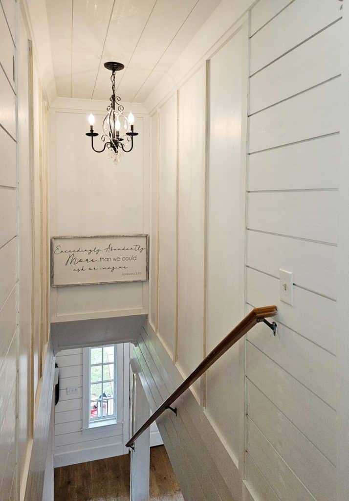 Area above stair well with board and batten walls and v-groove ceiling. Art piece and small chandelier.