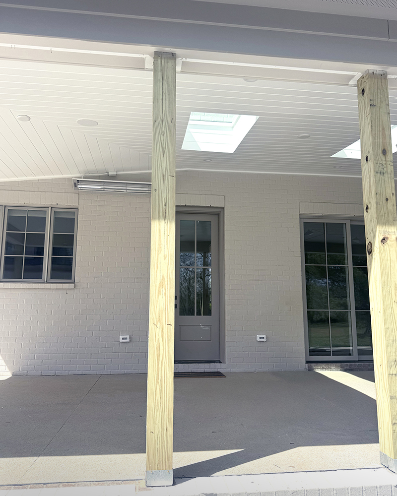 View of porch unfinished posts, v-groove exterior ceiling, gray door on tan brick