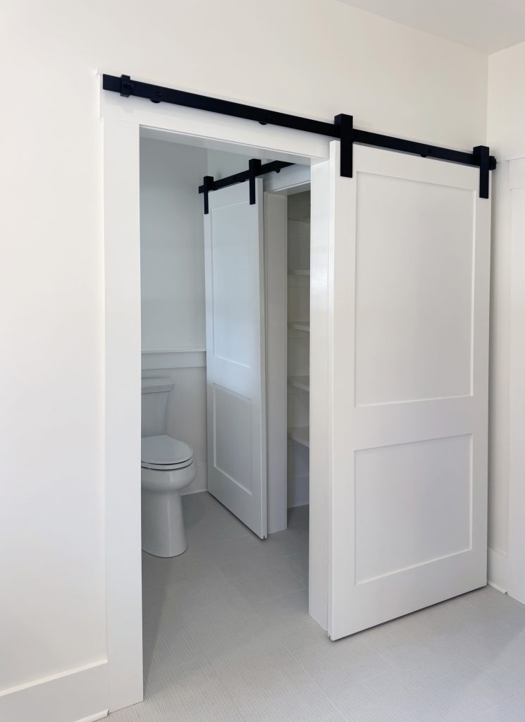 Shaker sliding barn door with black hardware leading to bathroom, simple farmhouse molding as the casing