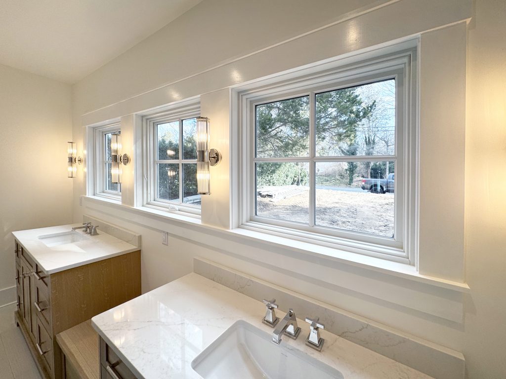 3 bathroom windows with 2 single sink vanities, farmhouse craftsman moldings, sconces mounted on trim