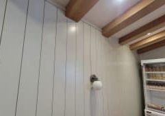 Shiplap wall painted light gray green, with light fixture and natural beams above